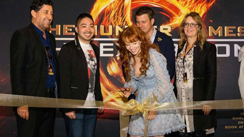 Stef Dawson surrounded by peers cutting a ribbon at an event for hunger games