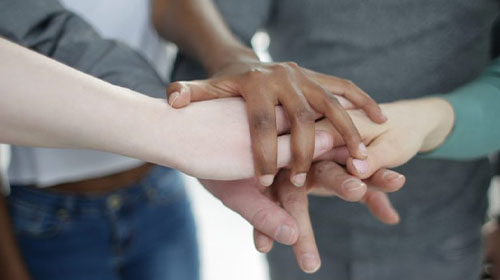 A stock photo of hands placed together at the centre of a team huddle.