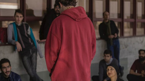 A photo of a man standing wearing a red hoodie surrounded by a group watching him