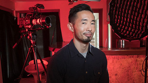 A photo of a Screenwise graduate smiling at the camera in the background a film set bathed in red light