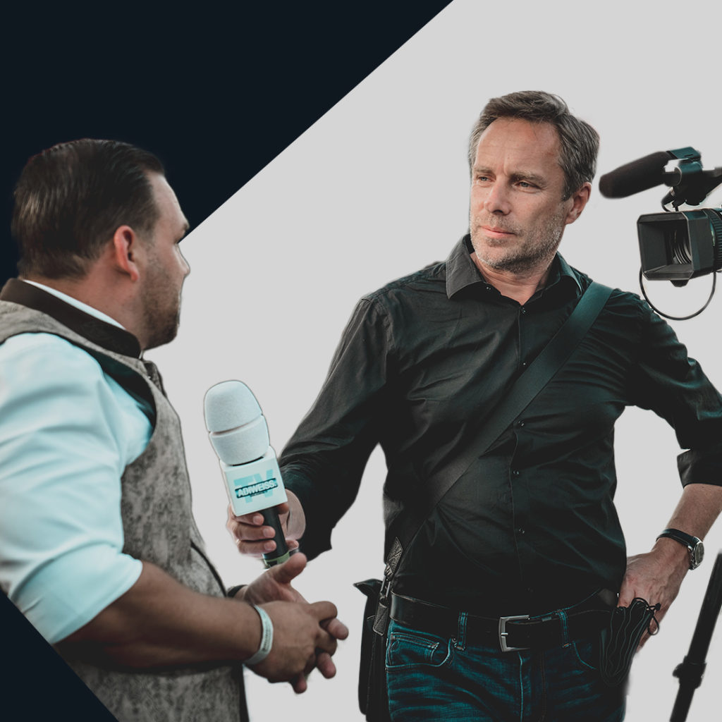 A television interviewer standing with a microphone next to a camera interviewing a man. The figures are cut-out and surrounded by triangular shutters, part of the Screenwise branding.